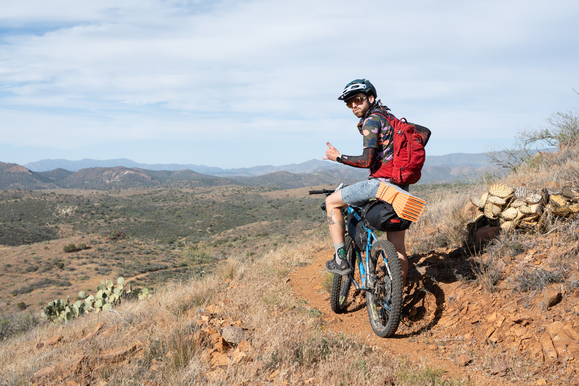 Bikepacker riding a narrow desert trail above a wide valley.