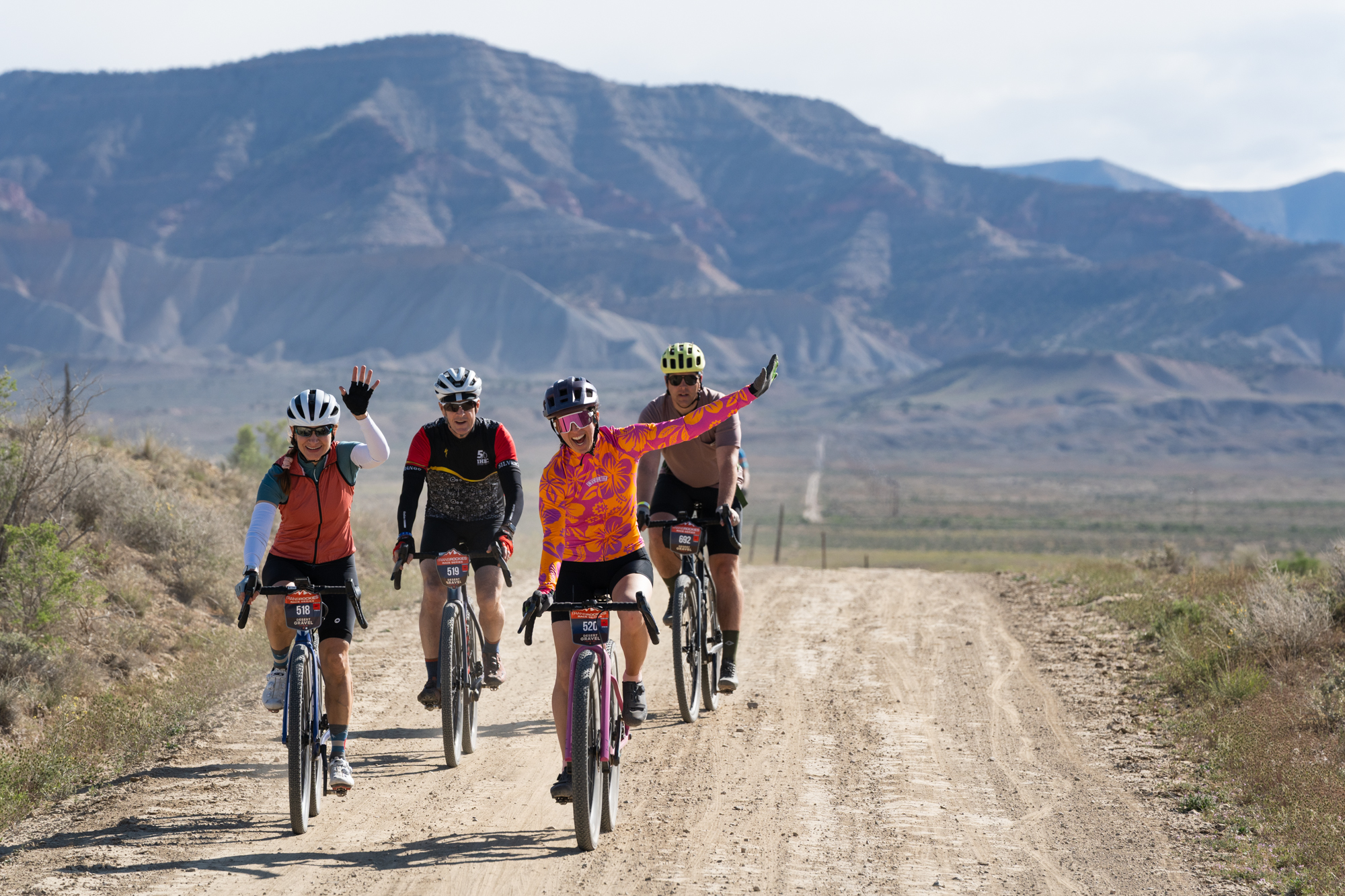 Four cyclists riding a gravel road with desert mountains behind them.