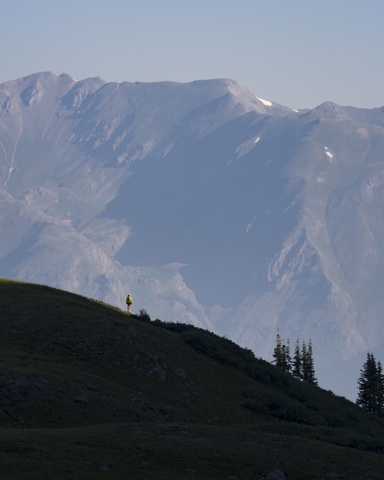 A lone runner crossing a dark ridge below a vast mountain face.