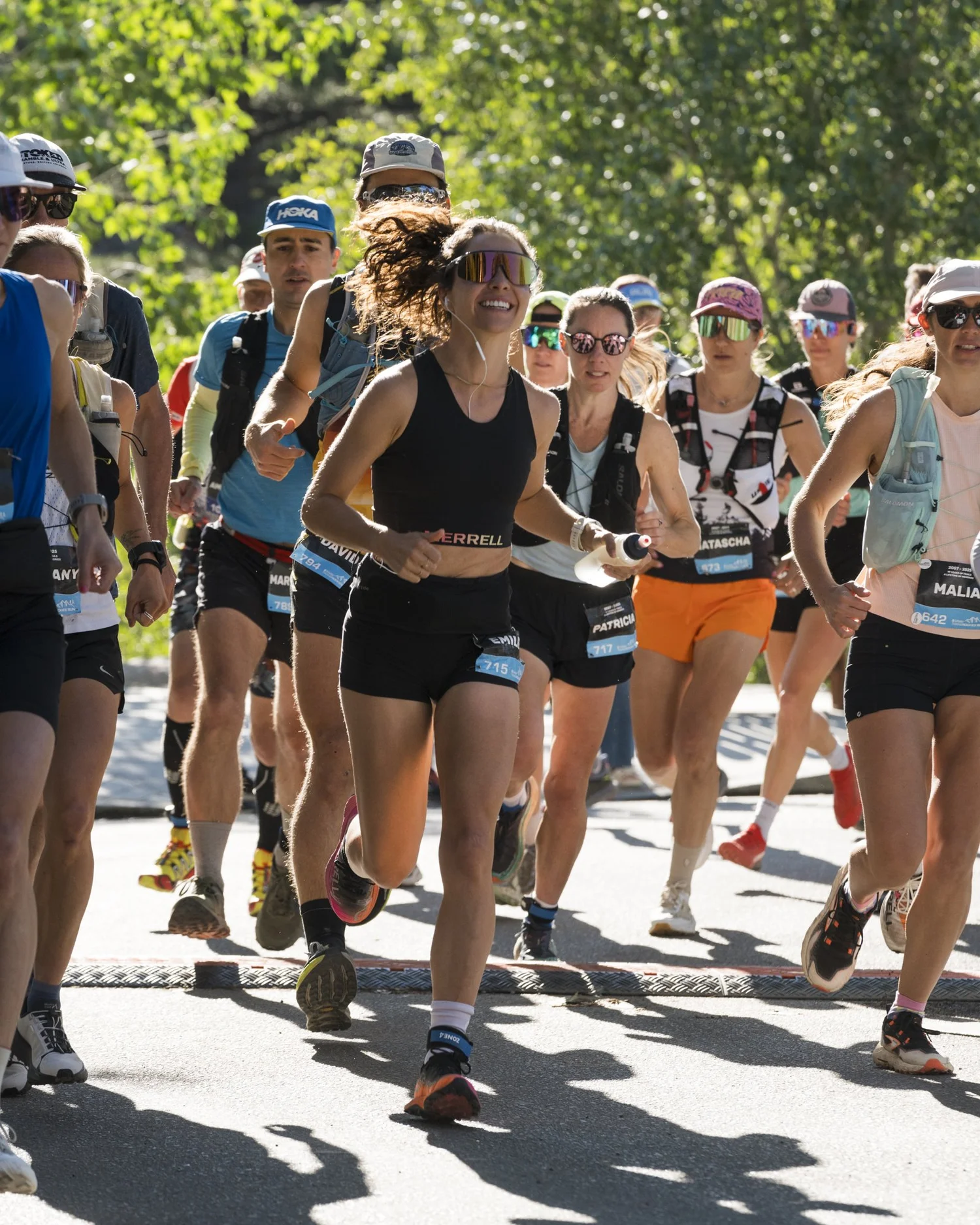 A pack of TransRockies runners crosses a stage start line in bright morning light.